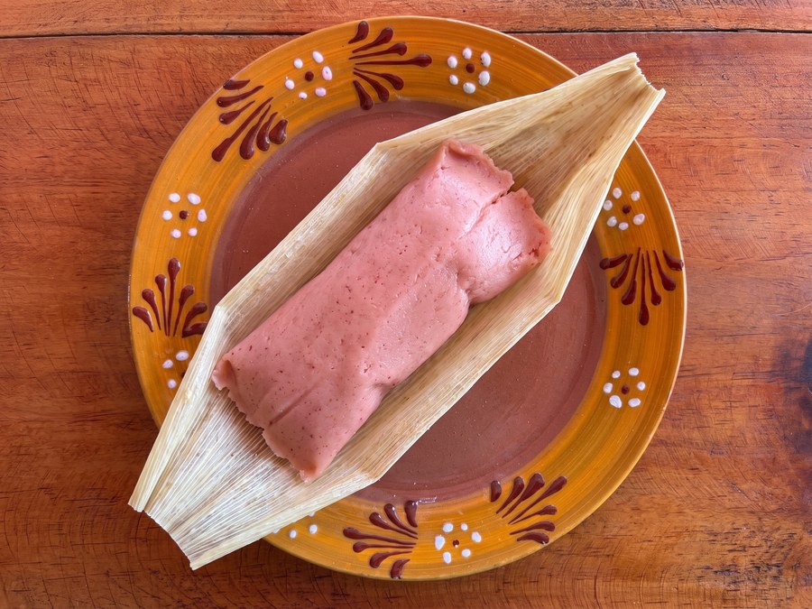 Tamal dulce con arándano (rosita) abierto en hoja de maíz, sobre plato de barro, visto desde arriba