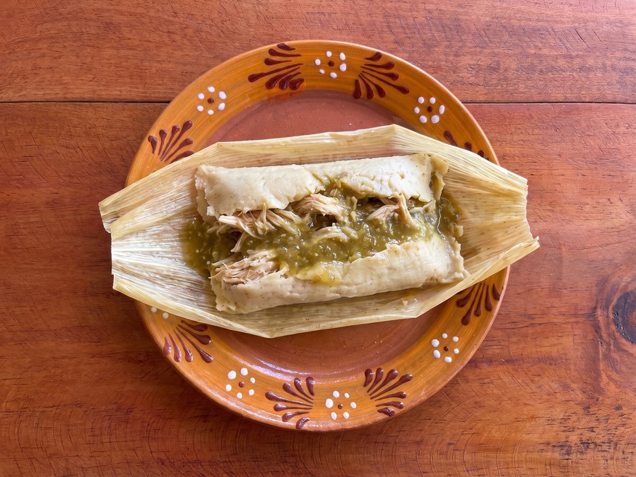 Tamal de salsa verde con pollo abierto en hoja de maíz, sobre plato de barro, visto desde arriba
