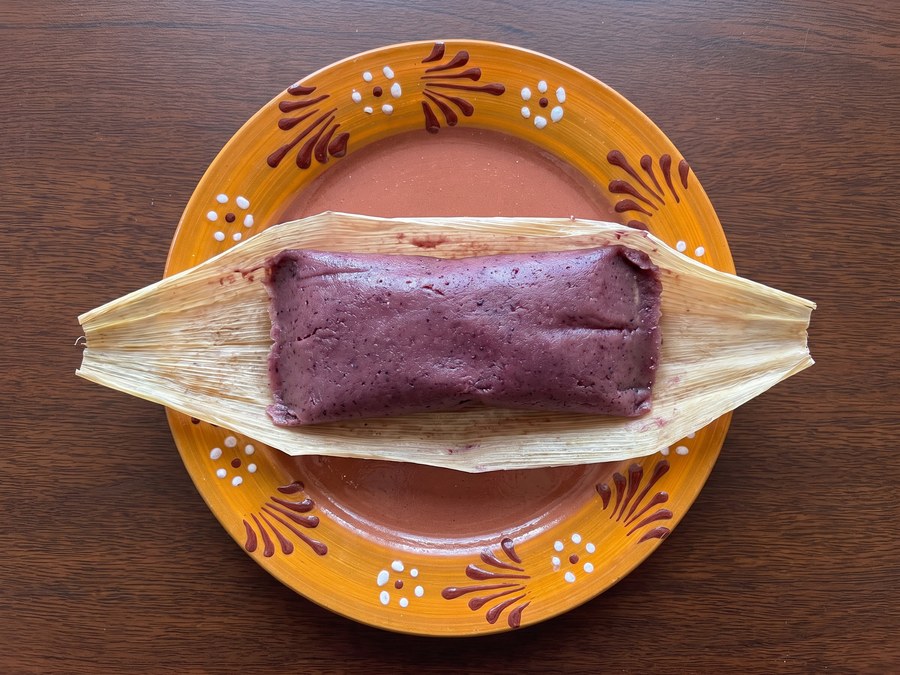 Tamal dulce de zarzamora con queso abierto en hoja de maíz, sobre plato de barro, visto desde arriba